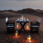 Desert camping setup with elegant table and lanterns in Moroccan sand dunes at dusk