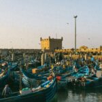 Fishing in Morocco - Traditional blue fishing boats docked in the harbor of Essaouira, Morocco, with the historic ramparts in the background.